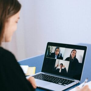 A woman participates in a virtual meeting with colleagues via video call on a laptop.