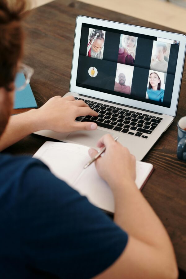 Person taking notes during a virtual meeting on a laptop screen with a diverse team.